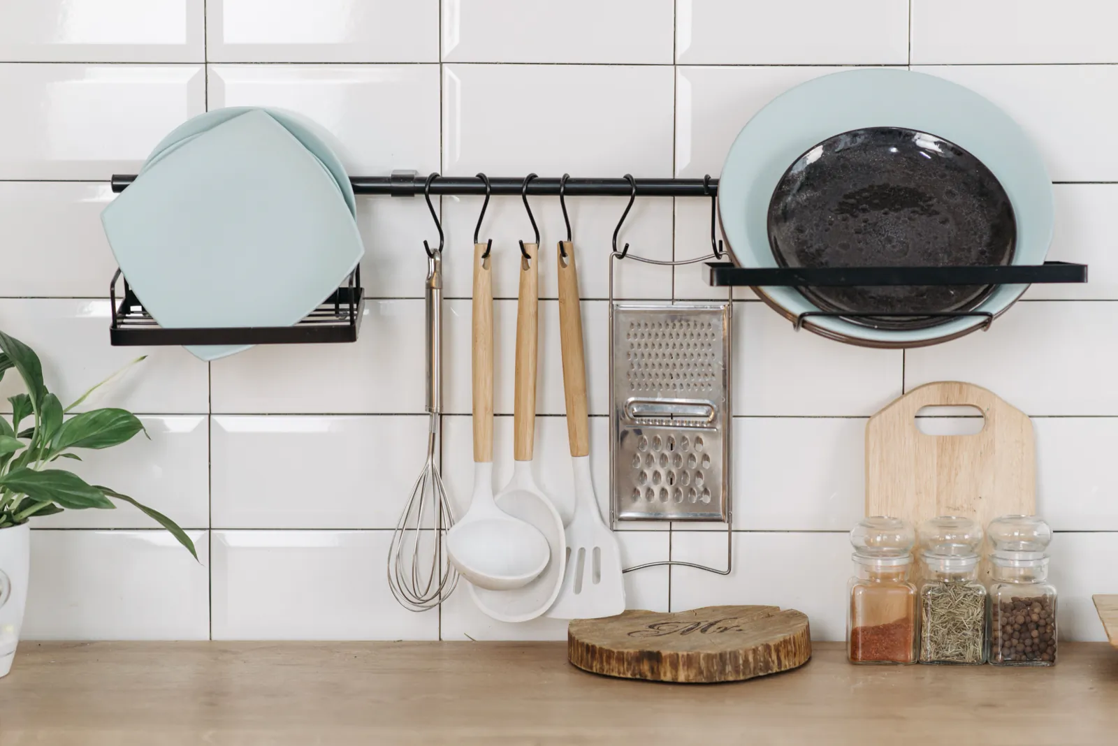 Kitchen utensils, plates and spice jars arranged on a white tiled wall